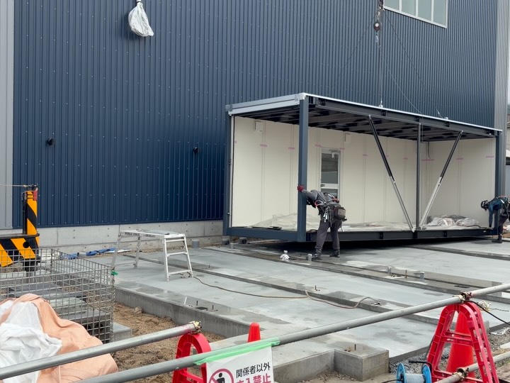 🏭 下松工場、事務所の設置が始まりました！ 以前「東洋鋼鈑の目の前で事務所の建設が始まります」とお伝えしましたが、 ついにその日がやってきました✨ 大きなユニットをクレーンで一つずつ吊り込み、 基礎の上にミリ単位で合わせて据え付けていきます🏗️ 曇り空の中でスタートした作業も、 気づけば青空の下、外観がしっかり見えるところまで！ ネイビーの外壁に、木目のルーバーがアクセント
